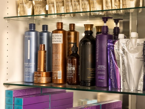 Glass bathroom shelves displaying an organized collection of hair care products in various colored bottles and white boxes