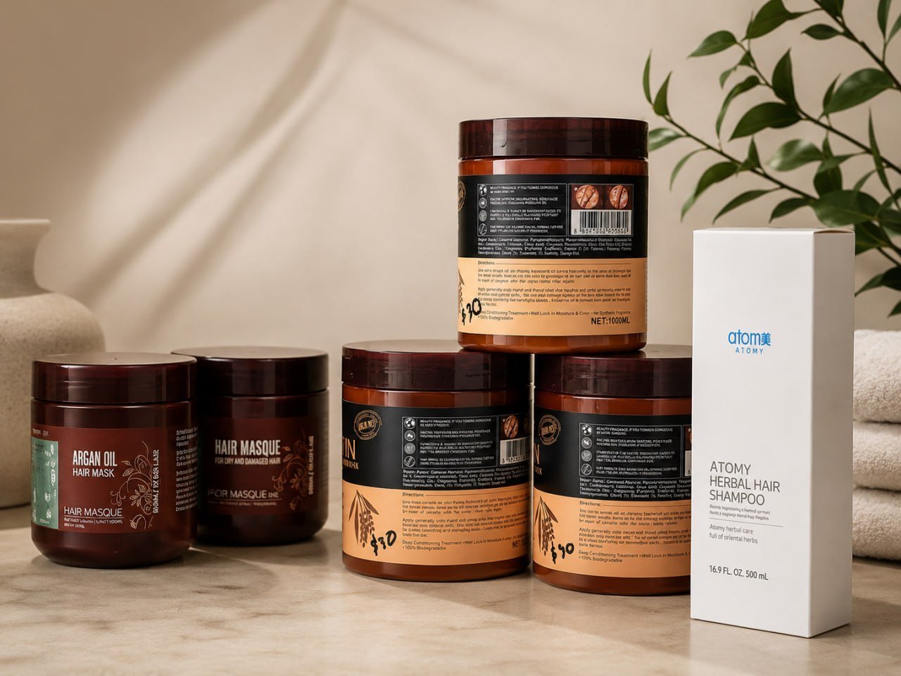 Collection of hair care products including jars and bottles arranged on a marble surface with plants and white towels in background
